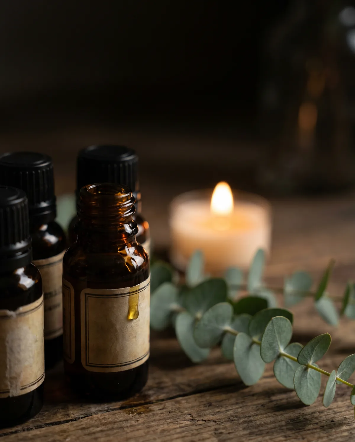 Amber bottles of essential oil beside a low candle flame and fresh eucalyptus.