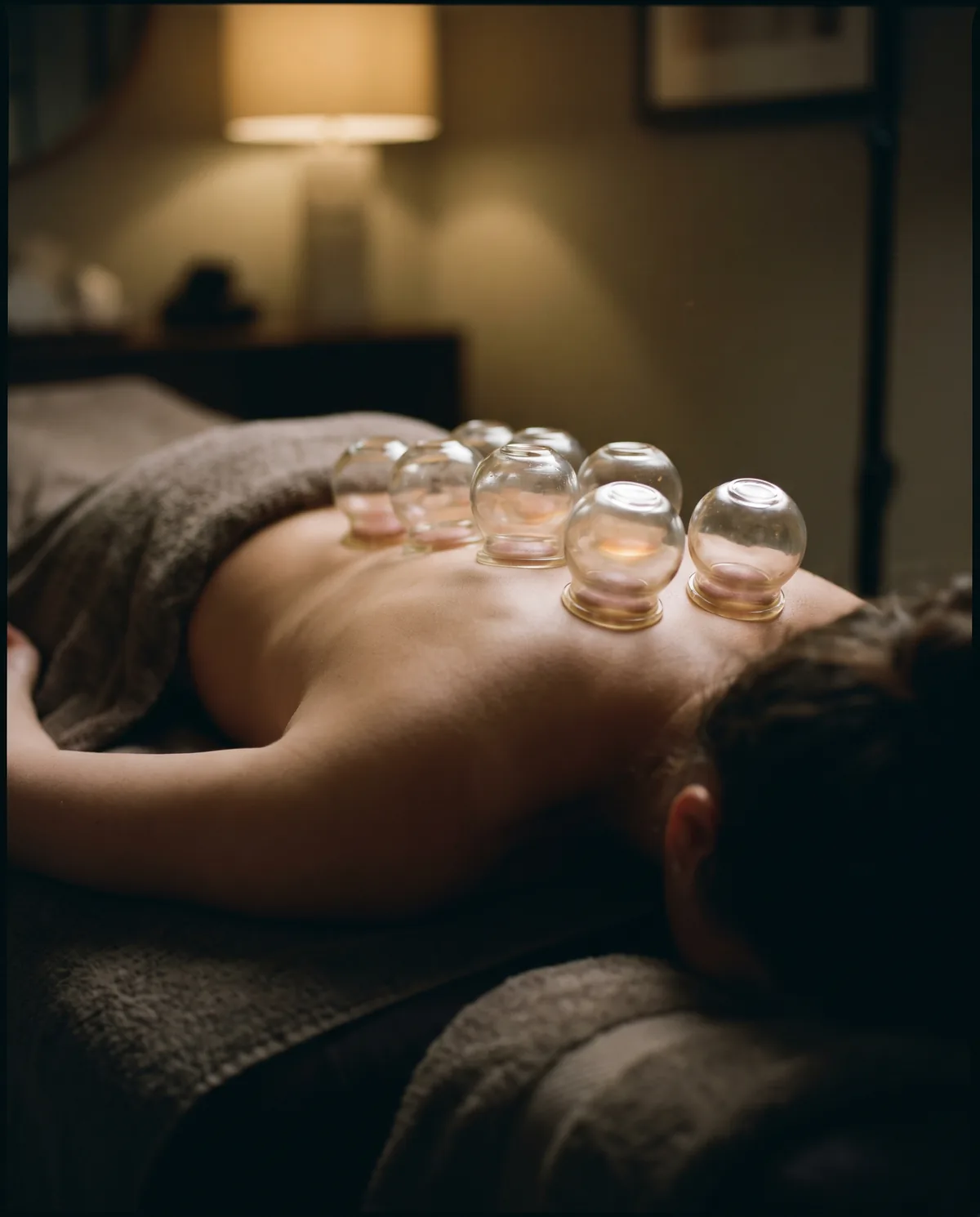 Glass cupping vessels along the upper back, each catching a ring of golden candlelight.