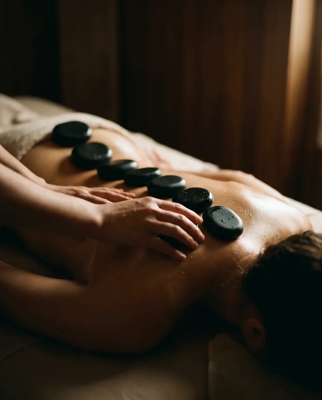Warm basalt stones resting along a client's back, candlelight catching the oil's sheen.